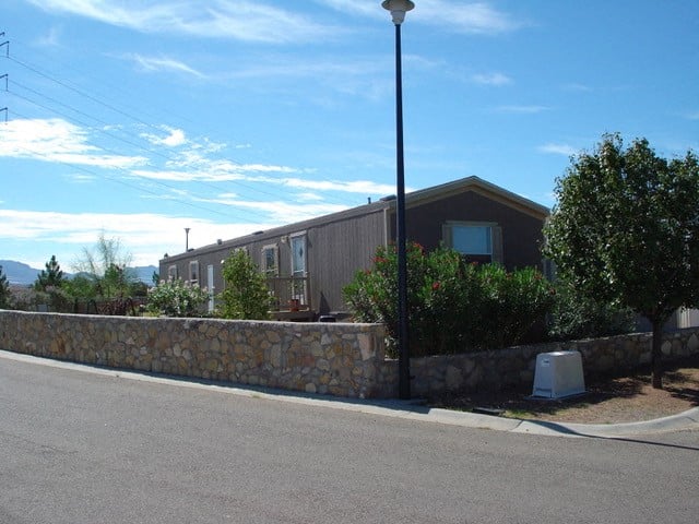 A street view with a house, a lamp post and a stone wall.